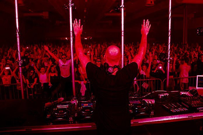 DJ u pultu sa podignutim rukama.